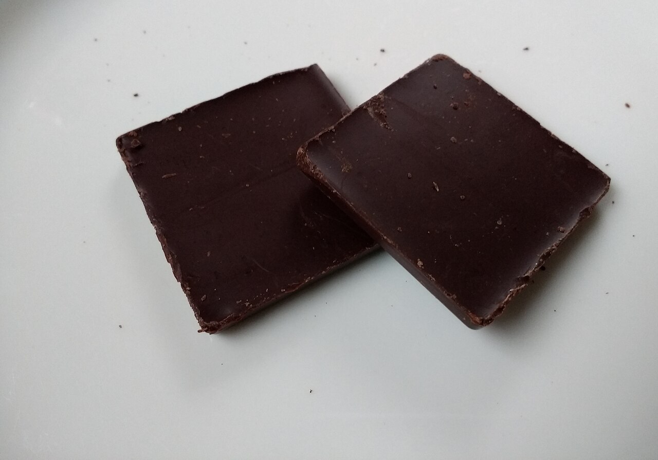 Two real pieces of dark chocolate photographed on a white surface